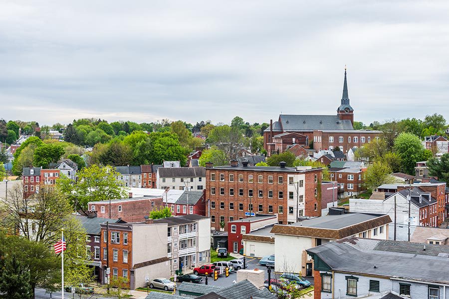 About Our Agency - Pennsylvania Town Seen From Above,With Church Spires, Brick Houses, Green Trees, and an American Flag Waving