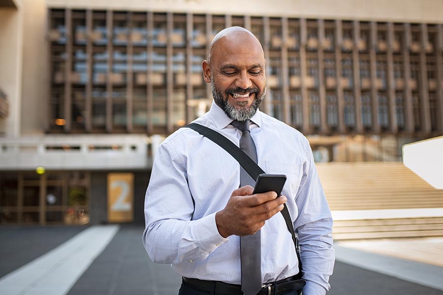 Contact Us - Businessman Smiles as He Checks His Phone Outside a Corporate Building