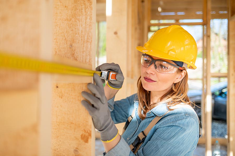 Specialized Business Insurance - Contractor in Hardhat and Safety Goggles Uses a Measuring Tape on a Job Site
